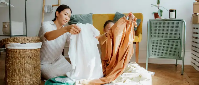 Mother and daughter sorting and folding laundry on the floor of a sunny living room