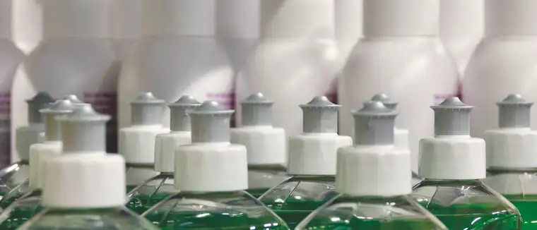 Rows of plastic cleaning bottles filled with green liquid and white caps