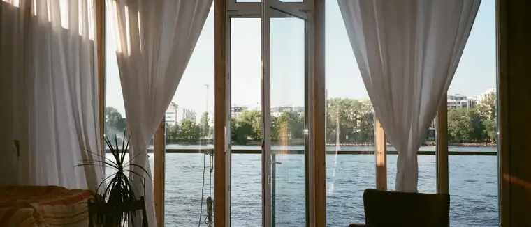 Living room with open glass doors and white curtains looking out over water
