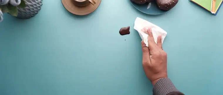 Hand blotting a chocolate spill with a tissue on a blue table