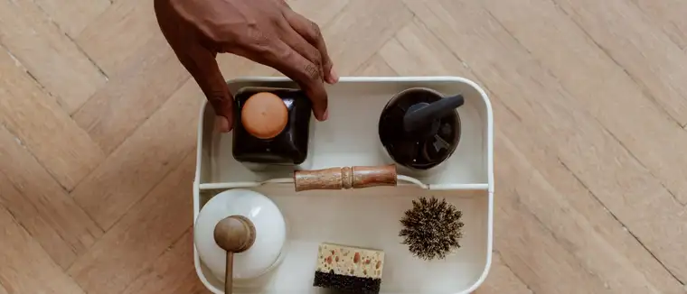 Hand reaching into a white cleaning caddy holding bottles, a brush and a sponge