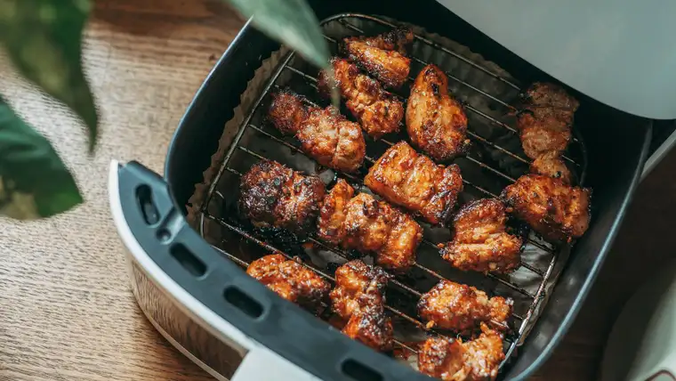 Open air fryer basket filled with crispy glazed chicken pieces on a wooden table