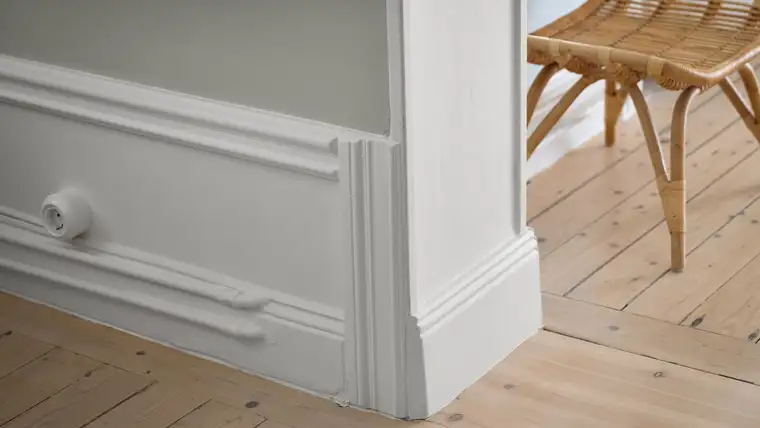 White painted baseboard and wall molding meeting pale pine floorboards