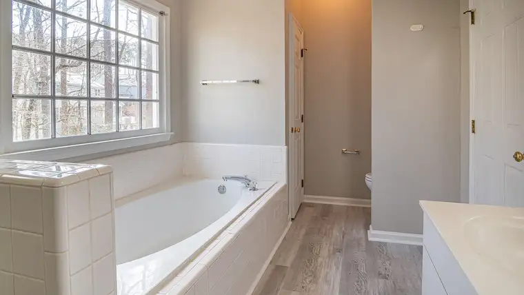 Clean white drop-in bathtub with tiled surround under a large bright window