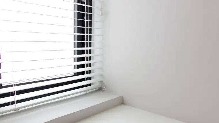 White horizontal window blinds lowered over a bright window above a sill