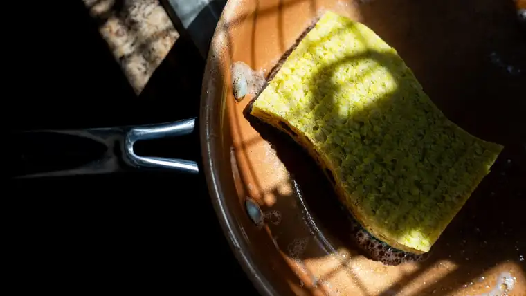 Yellow sponge soaking in soapy water inside a copper-colored frying pan