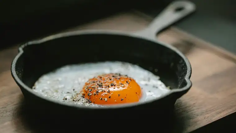 Black cast iron skillet with a fried egg on a wooden board