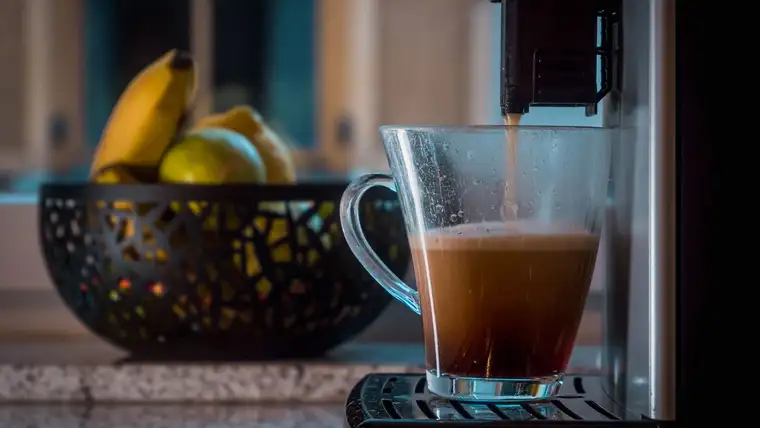 Coffee machine dispensing coffee into a glass mug beside a bowl of fruit