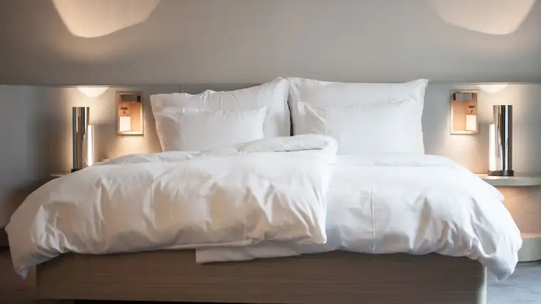 Fluffy white duvet and pillows on a neatly made bed in a softly lit bedroom