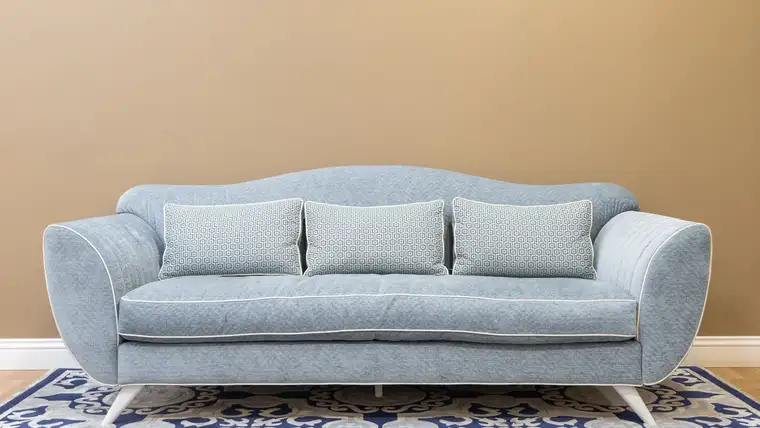Light blue fabric sofa with matching cushions against a beige wall