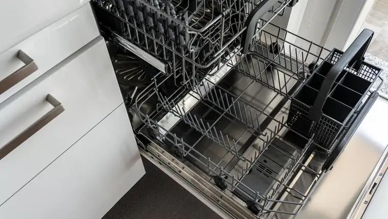 Open empty dishwasher with pulled-out wire racks beside white kitchen cabinets