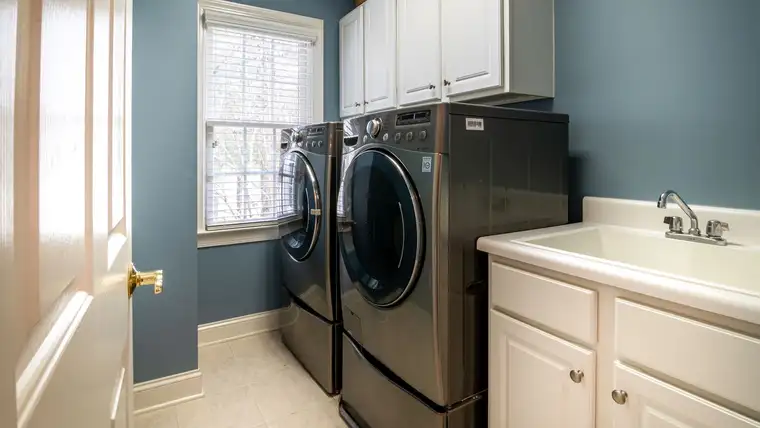 Front-loading washer and dryer pair beside a utility sink in a blue laundry room