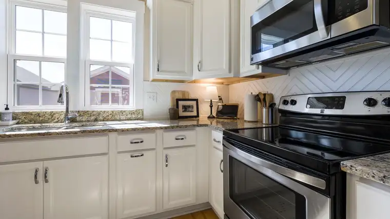 White shaker kitchen cabinets above a stove, microwave and stone countertop