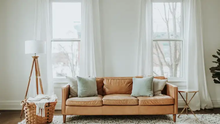 Tan leather sofa with pillows on a white rug in a bright living room