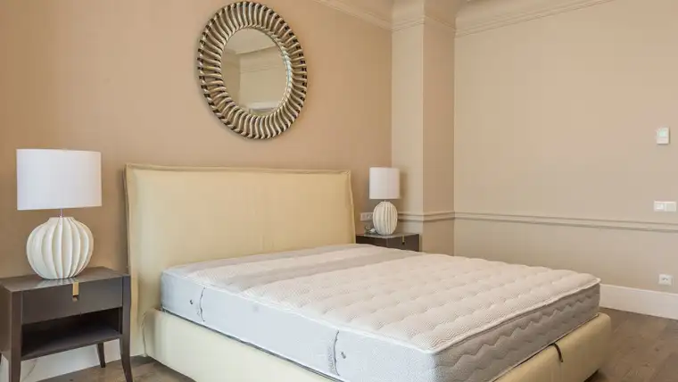 Bare white quilted mattress on a cream upholstered bed frame in a bedroom