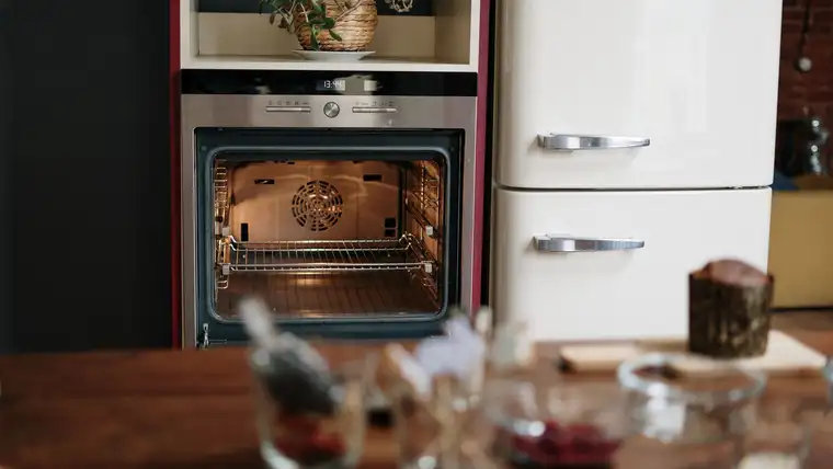 Open built-in oven with lit interior and wire racks beside a cream refrigerator