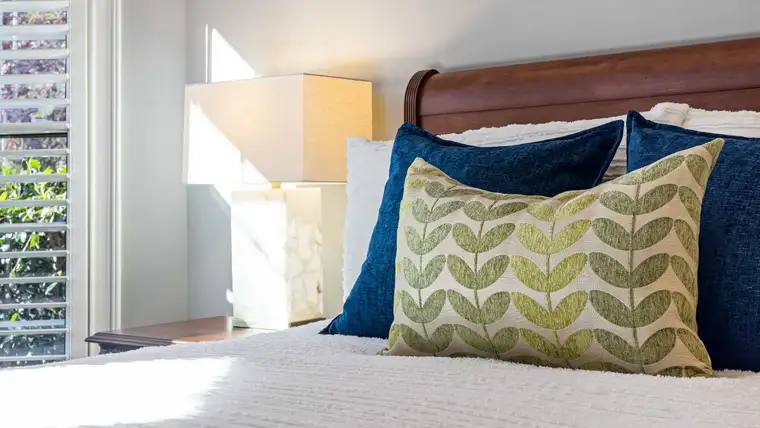 Navy and leaf-patterned throw pillows stacked against a headboard on a made bed