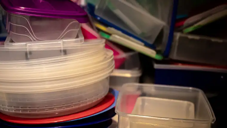 Stack of clear and colored plastic food storage containers with lids in a cupboard
