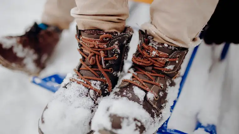 Brown leather winter boots caked with snow resting on a blue sled