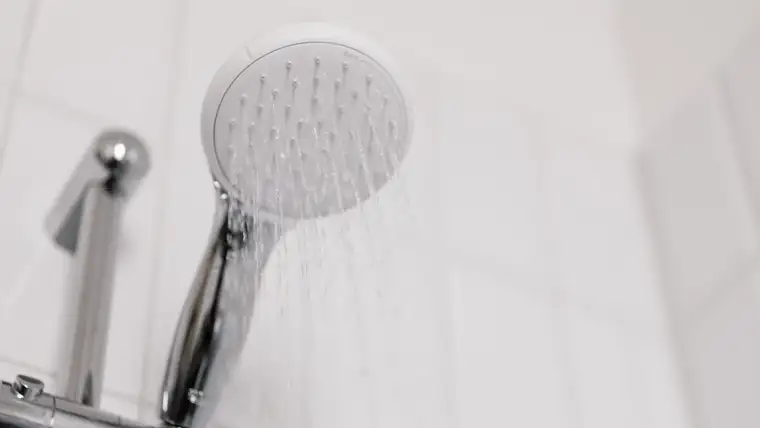 Chrome handheld shower head spraying water against white bathroom tiles