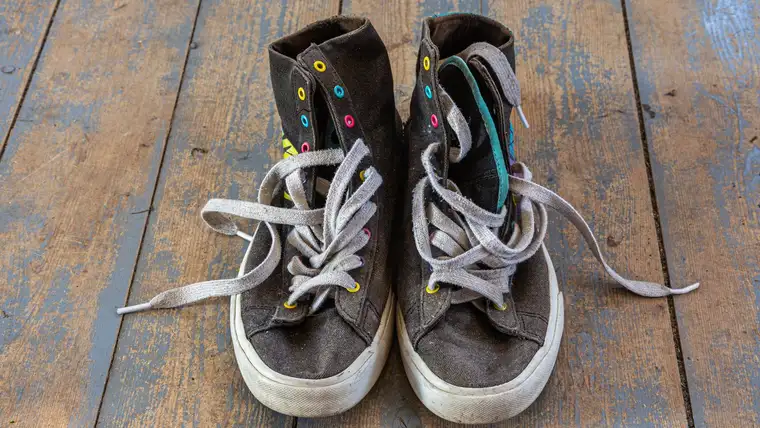 Well-worn dark canvas high-top sneakers with loose laces on old floorboards