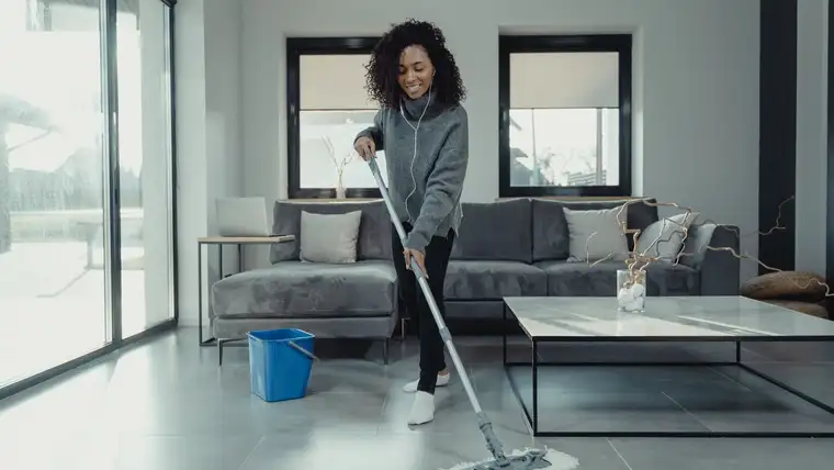 Woman mopping a large gray tile floor in a bright modern living room