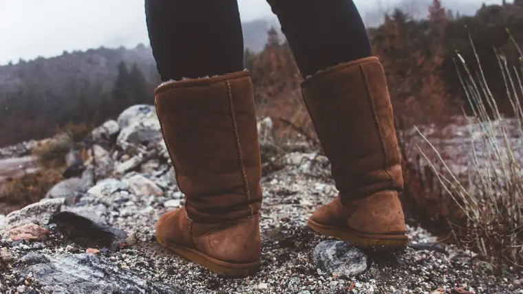 Tall brown sheepskin boots standing on rocky ground on a misty day