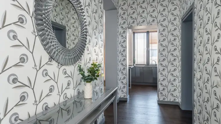 Hallway covered in gray and white leaf-patterned wallpaper with a round mirror