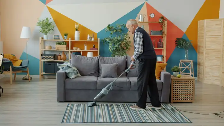 Colorful geometric painted accent wall behind a gray sofa as a man vacuums