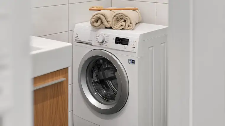 White front-loading washing machine with folded towels on top in a bright bathroom