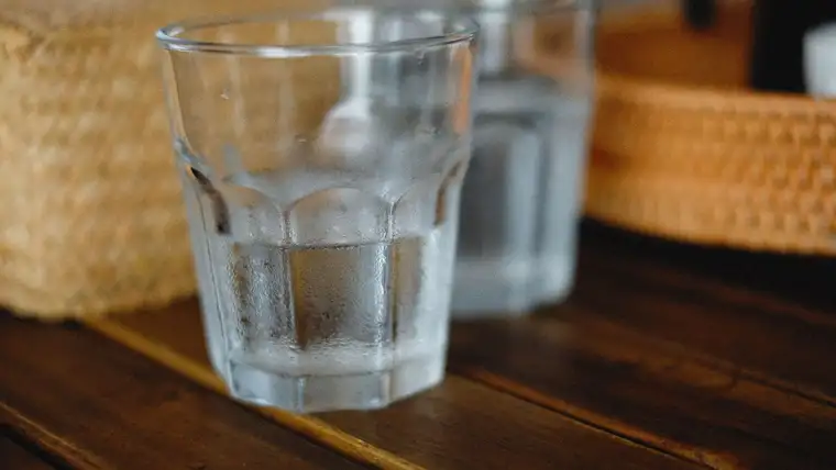 Cold glass of water with condensation sitting directly on a dark wooden table
