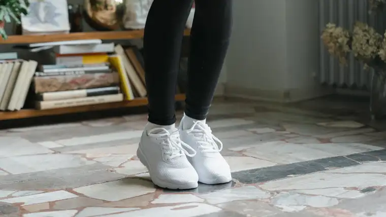 Person in black leggings wearing clean all-white mesh sneakers on a stone floor