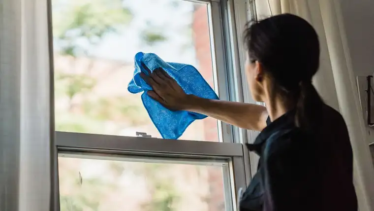 Woman wiping a sash window pane with a blue microfiber cloth