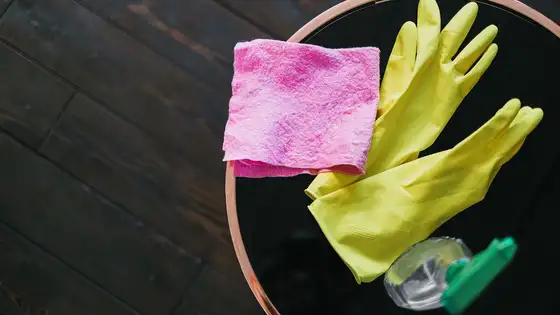 Yellow rubber gloves, a pink cleaning cloth and a spray bottle on a table