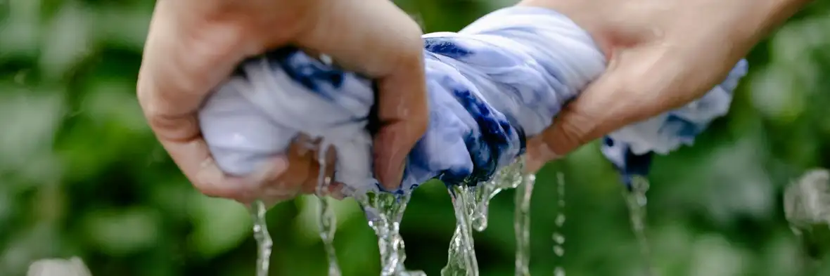 Hands wringing water out of a blue and white dyed garment outdoors