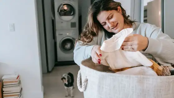 Woman sorting laundry from a fabric basket in front of a stacked washer and dryer