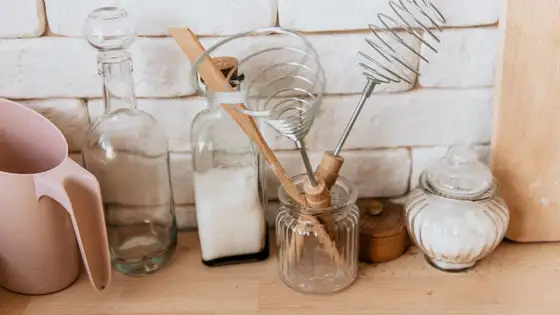 Glass bottle, jars of white powder and whisks on a wooden kitchen counter
