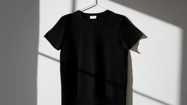 Plain black cotton T-shirt on a white hanger against a sunlit wall