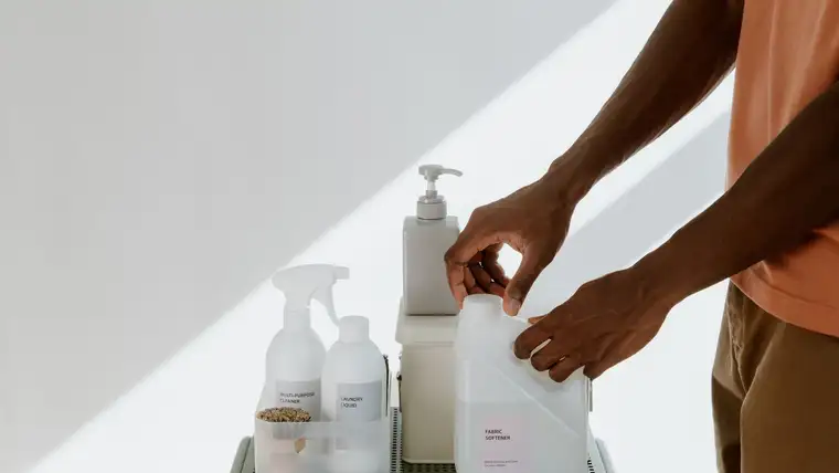 Hands setting a jug of fabric softener beside laundry liquid and cleaner bottles