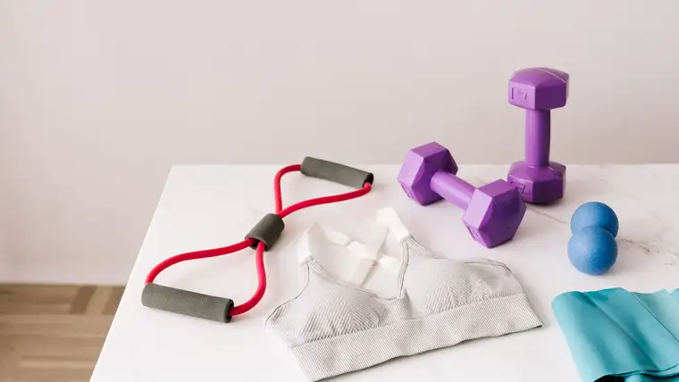 White sports bra on a table beside dumbbells, a resistance band and massage ball