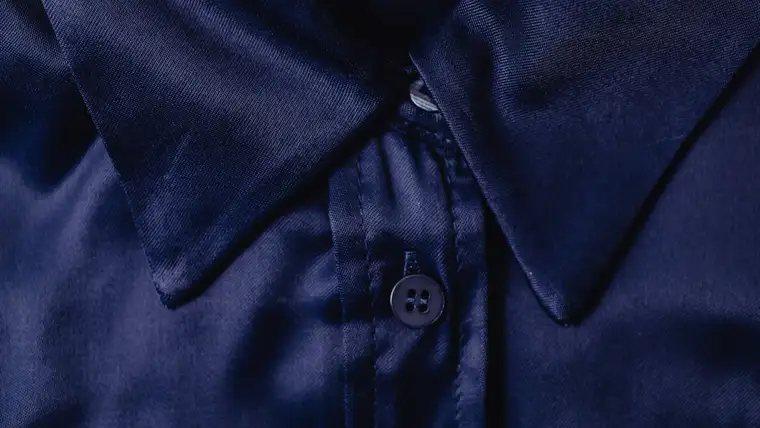 Close-up of a navy silk shirt collar and button showing the fabric's sheen