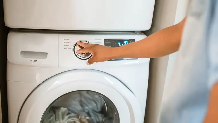 Hand turning the cycle dial on a front-loading washing machine with clothes inside