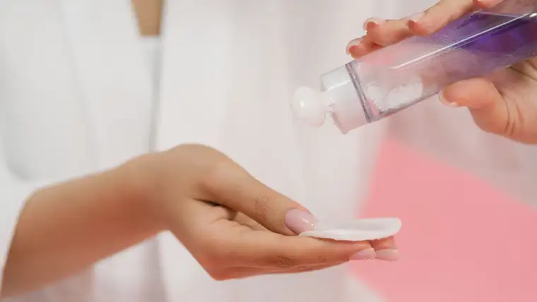 Hands pouring nail polish remover from a clear bottle onto a cotton pad