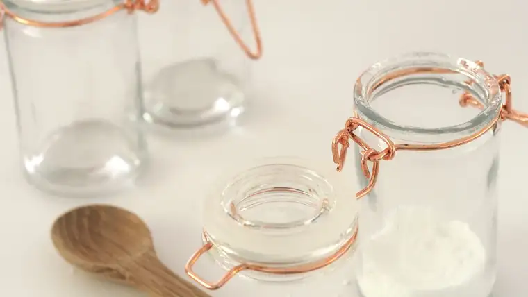 Small glass jar of white baking soda powder beside an empty jar and wooden scoop
