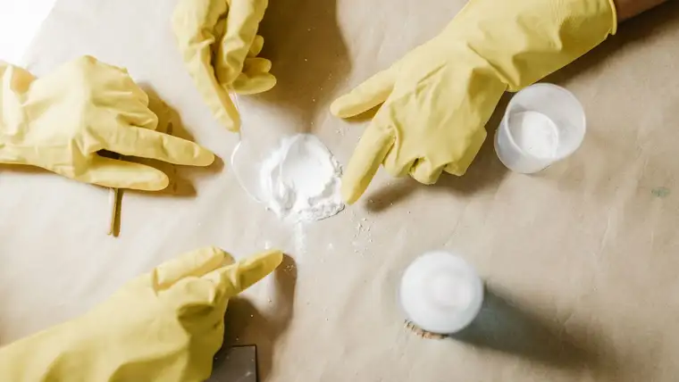 Gloved hands measuring a fine white cleaning powder with a spoon on paper