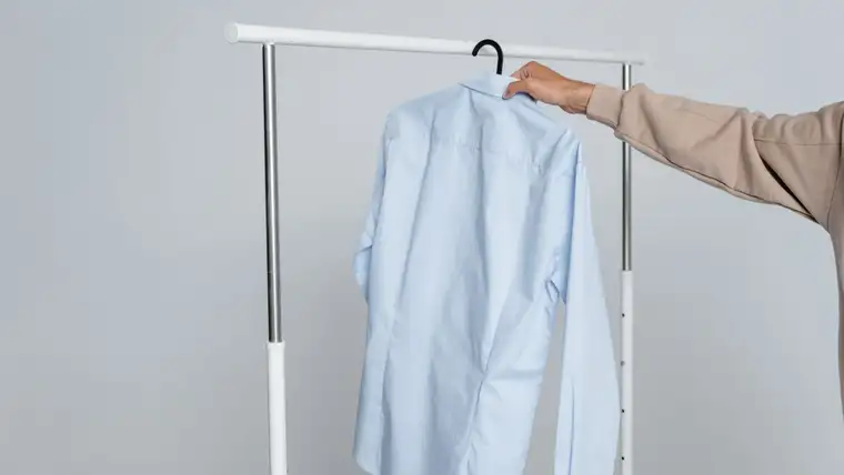 Hand hanging a pale blue dress shirt on a clothing rack