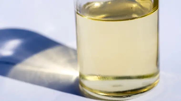 Clear glass bottle of thick pale yellow glycerin casting a shadow on white
