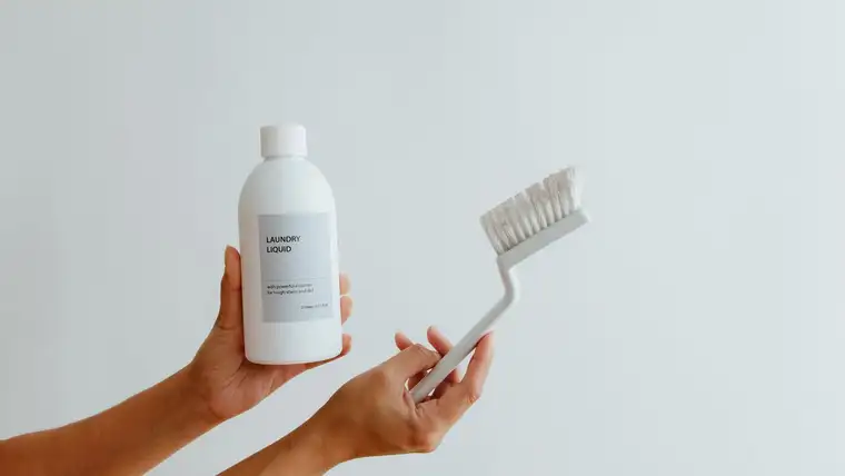 Hands holding a bottle of enzyme laundry liquid and a stain scrub brush