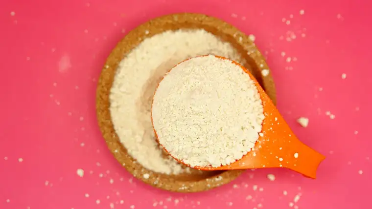 Orange measuring scoop filled with powdered laundry detergent over a dish