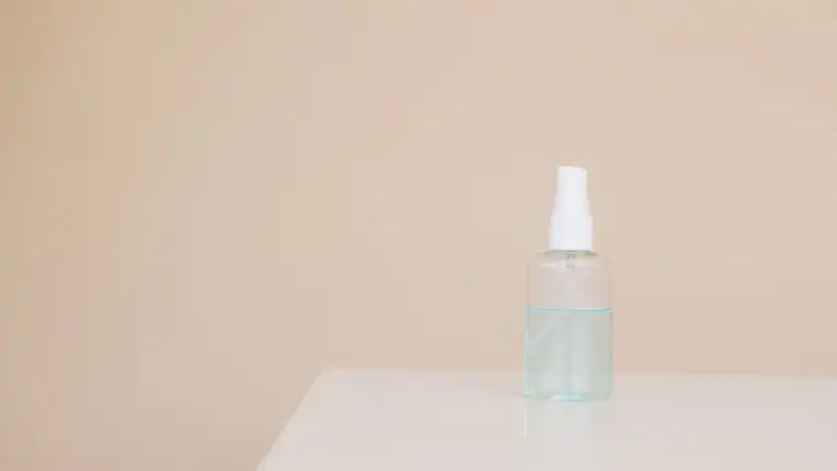 Small clear spray bottle of alcohol solution on a white table